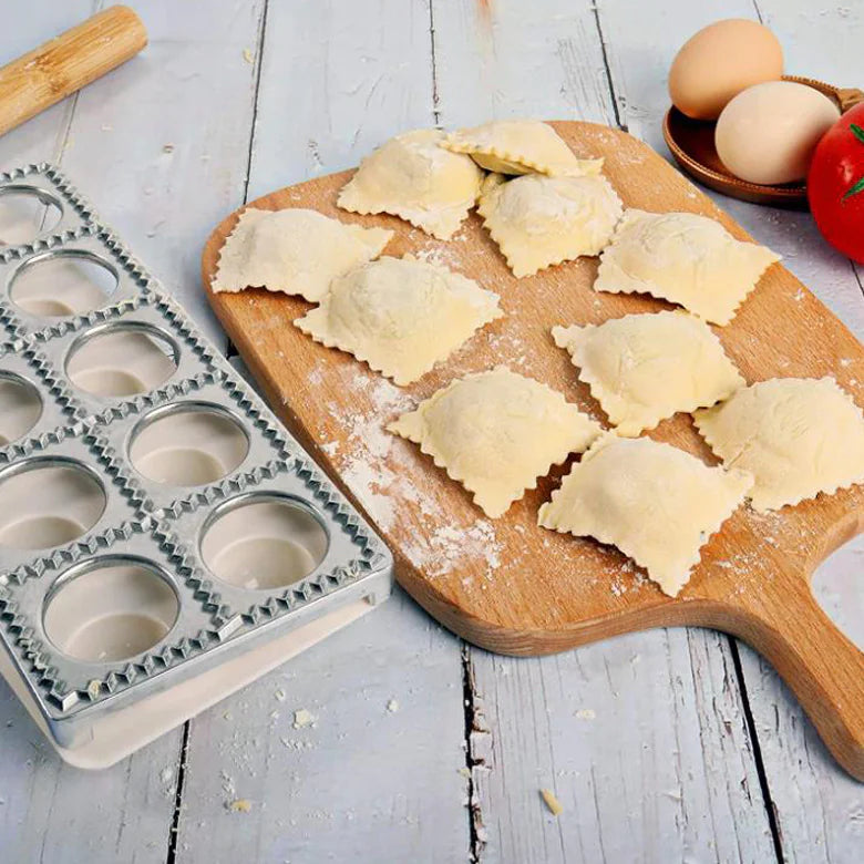 Metal ravioli mold tray next to finished ravioli on a cutting board