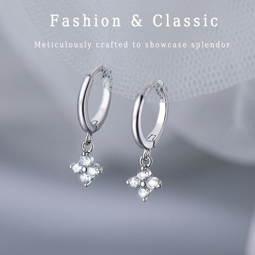Silver-tone huggie hoop earrings with dangling four-leaf clover charms on a fabric background