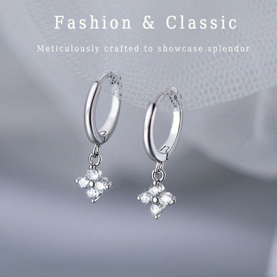 Silver-tone huggie hoop earrings with dangling four-leaf clover charms on a fabric background