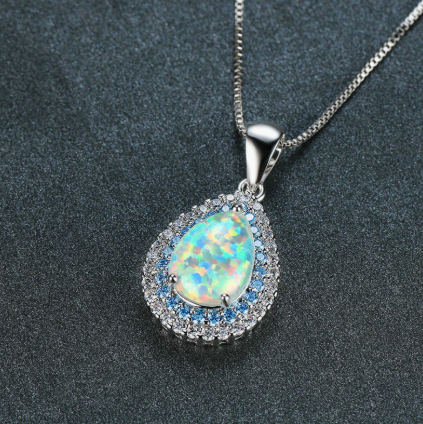 Close-up of teardrop opal pendant with blue and clear crystal halo on silver chain