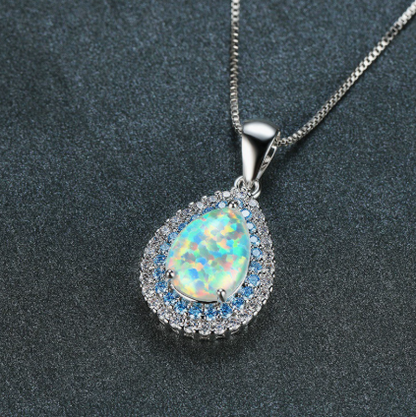 Close-up of teardrop opal pendant with blue and clear crystal halo on silver chain