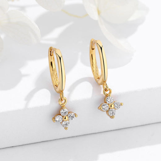 Close-up of gold-tone four-leaf clover charm earrings with clear stone accents