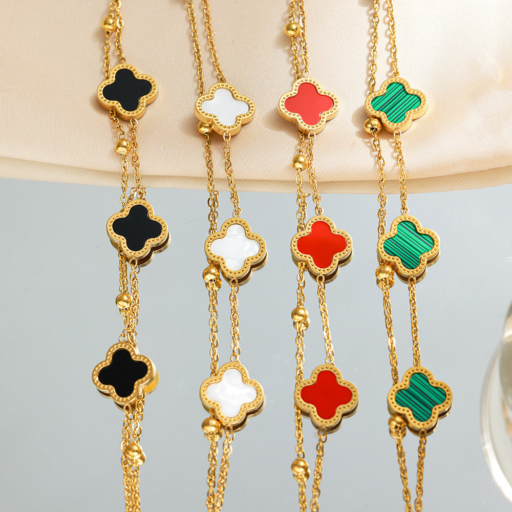Four gold-tone clover bracelets in black, white, red and green on a fabric