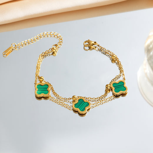 Green four-leaf clover charm bracelet with gold-tone double chain and lobster clasp, flat lay