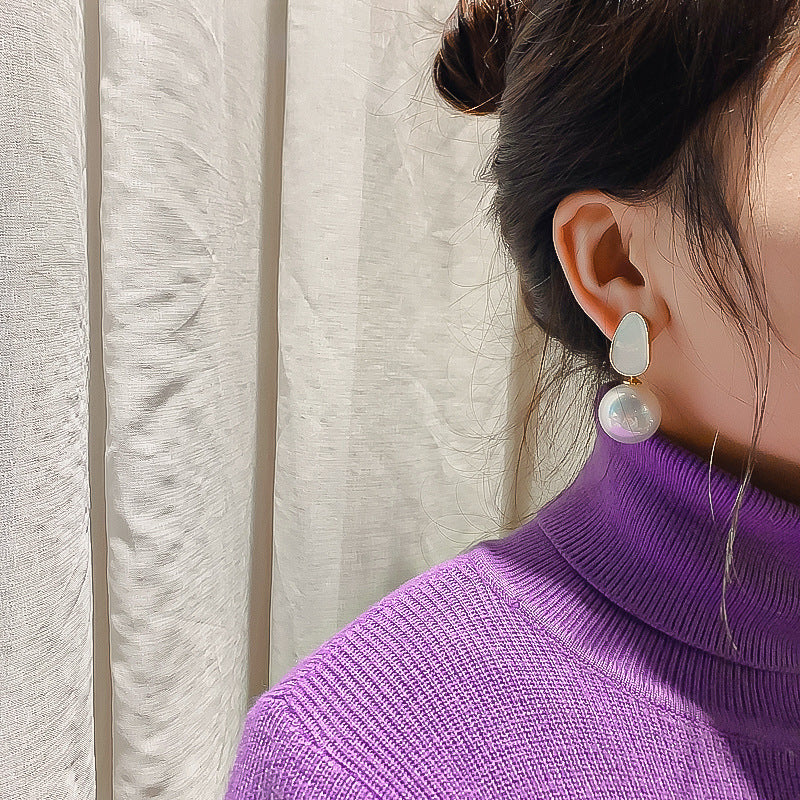 Woman wearing a pink pearl drop stud earring with a purple sweater, close-up side view