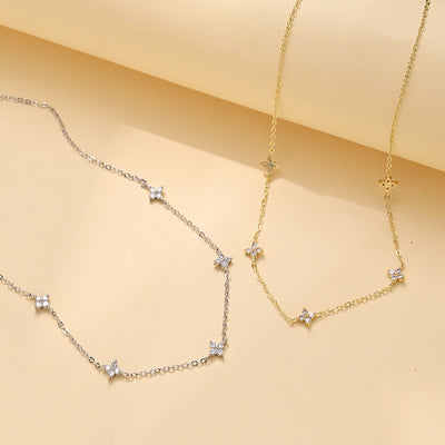 White gold-tone and gold-tone clover station necklaces laid side by side on a tan surface