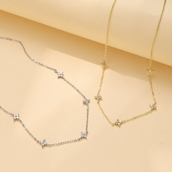 Gold and silver tone station necklaces with four-petal crystal charms on beige fabric