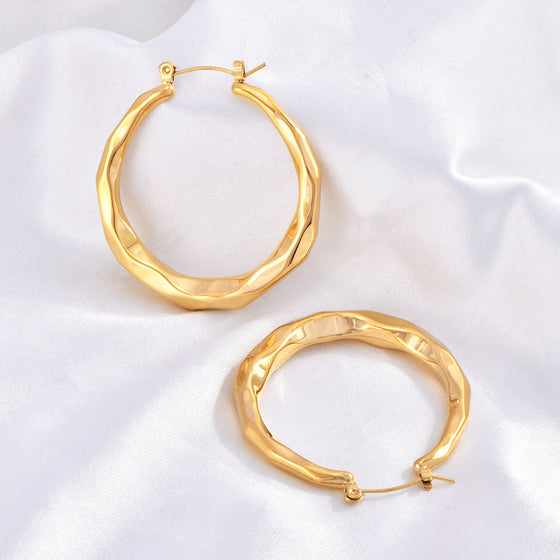 Top-down view of two wavy gold hoop earrings showing the hinged post closures