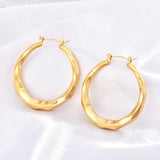 Angled close-up of gold titanium steel hoop earrings highlighting the wavy ring design