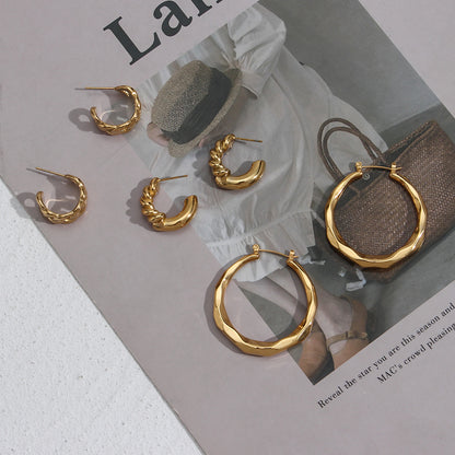 Pair of gold-tone titanium steel twisted hoop earrings laid on a white surface