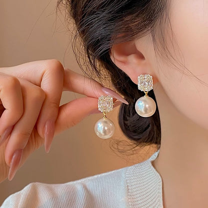Woman wearing a gold-tone square zircon and faux pearl drop stud earring