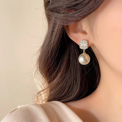 Close-up of a gold-tone square zircon cluster stud earring with pearl drop worn on the ear