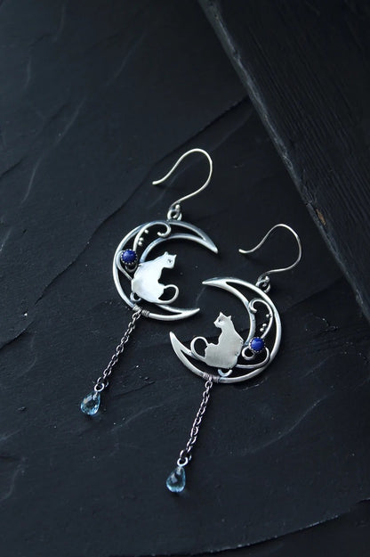 Close-up of alloy crescent moon cat charm dangle earring showing chain and blue bead drop detail