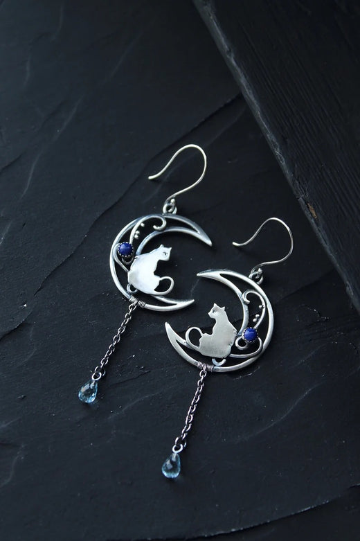 Close-up of alloy crescent moon cat charm dangle earring showing chain and blue bead drop detail