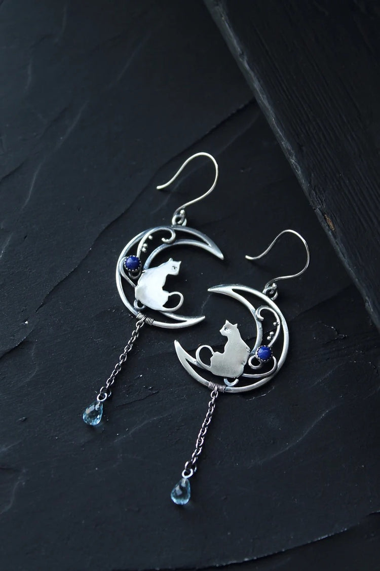 Close-up of alloy crescent moon cat charm dangle earring showing chain and blue bead drop detail