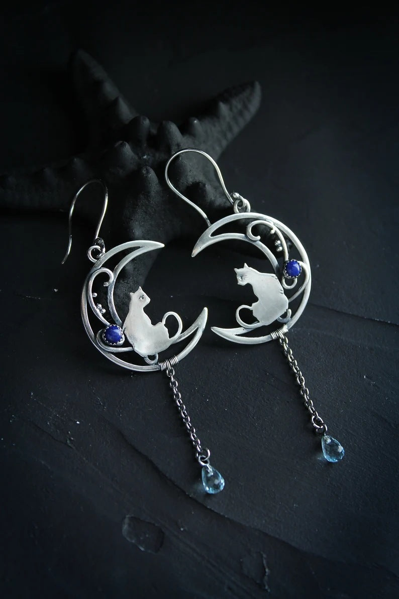 Pair of Moon Kitten dangle earrings on dark slate with a black starfish styling prop