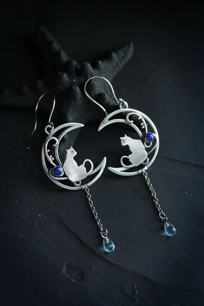 Pair of Moon Kitten dangle earrings on dark slate with a black starfish styling prop