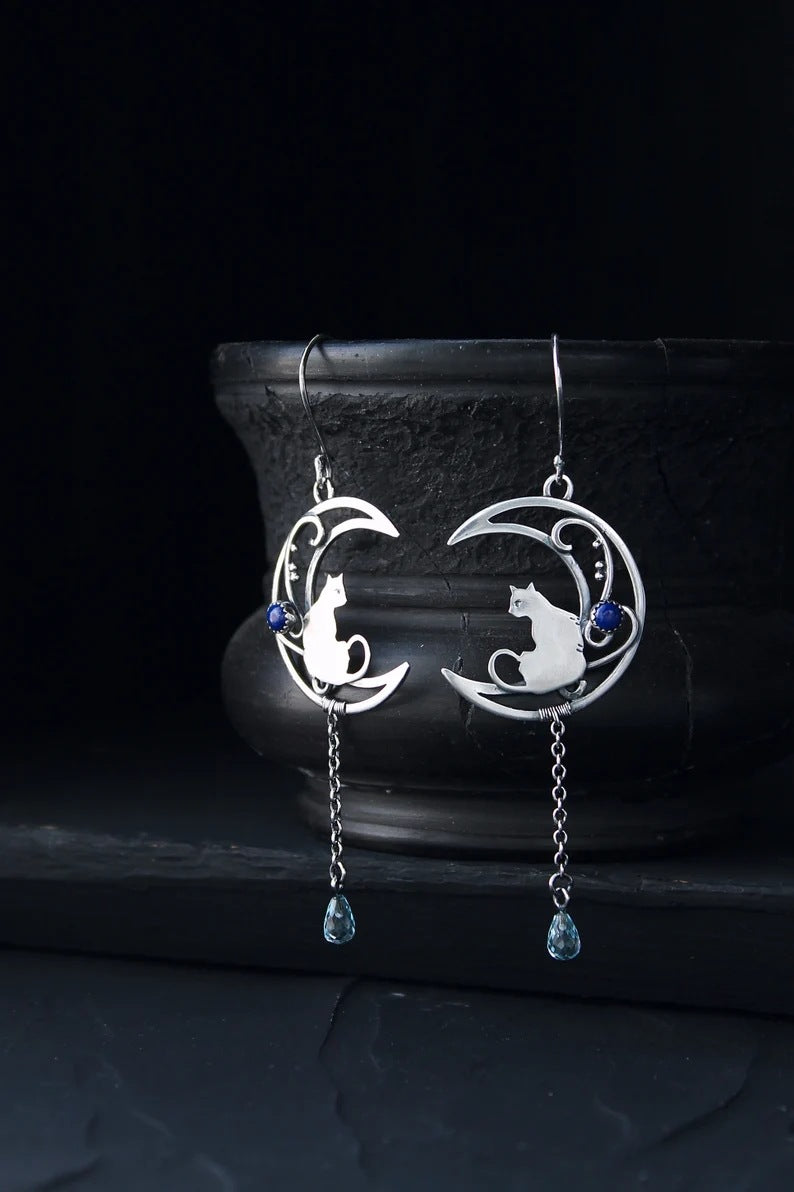 Moon Kitten dangle earrings displayed upright against a dark ceramic vase