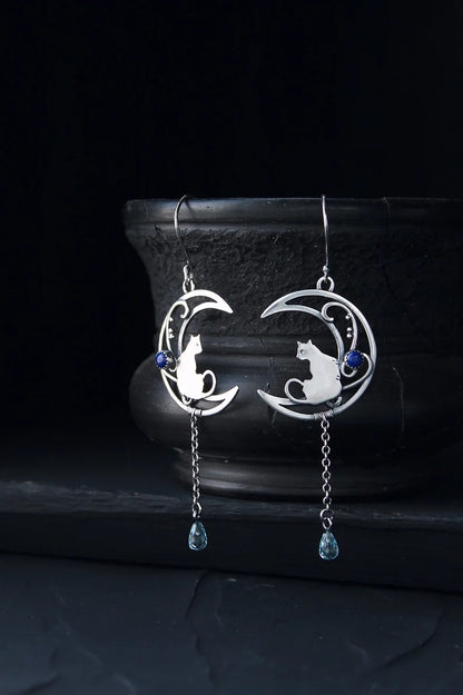 Moon Kitten dangle earrings displayed upright against a dark ceramic vase