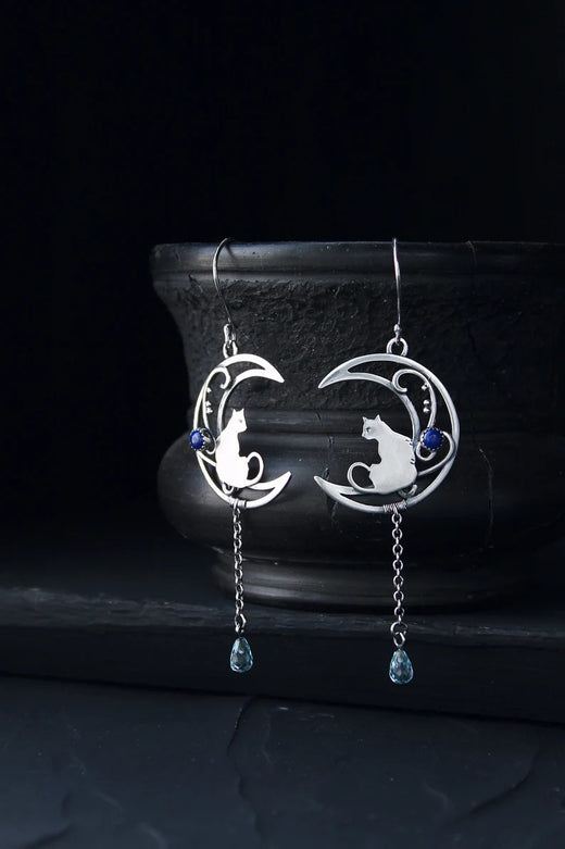 Moon Kitten dangle earrings displayed upright against a dark ceramic vase