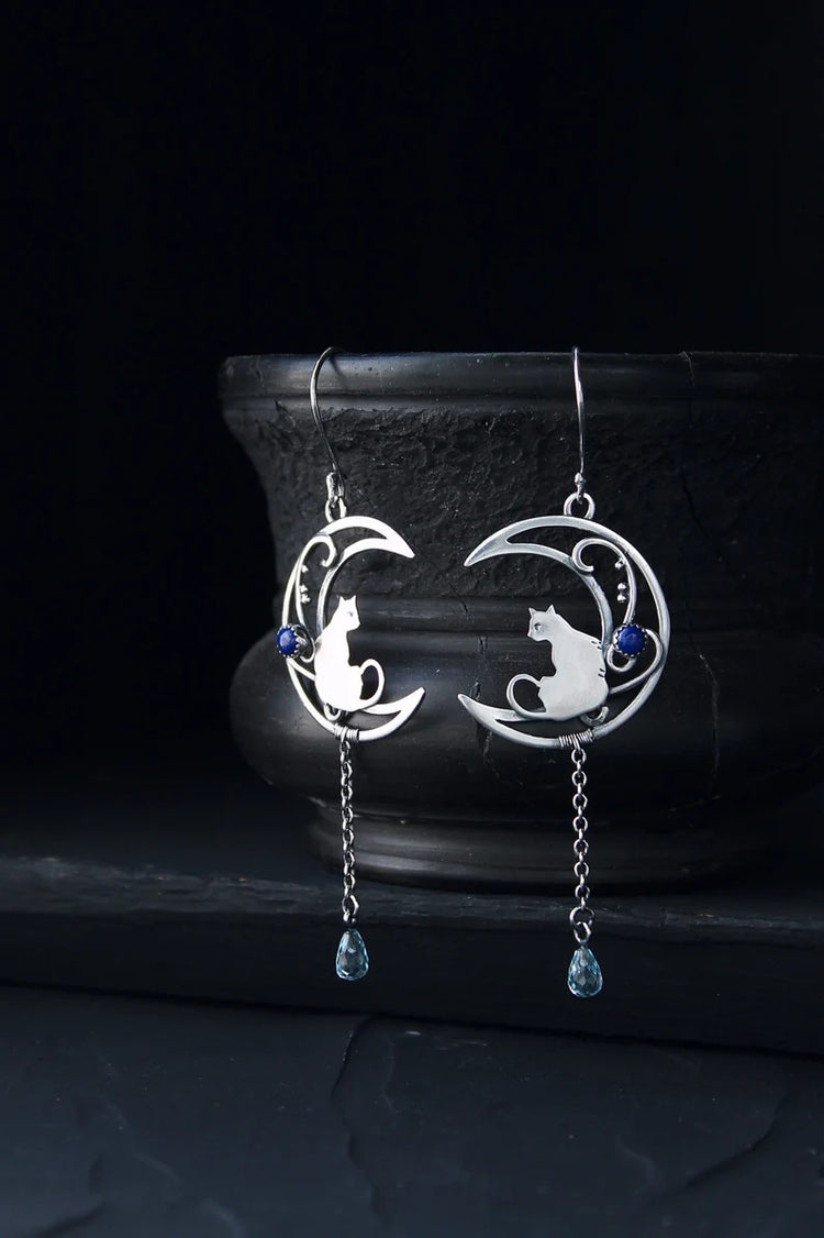 Moon Kitten dangle earrings displayed upright against a dark ceramic vase