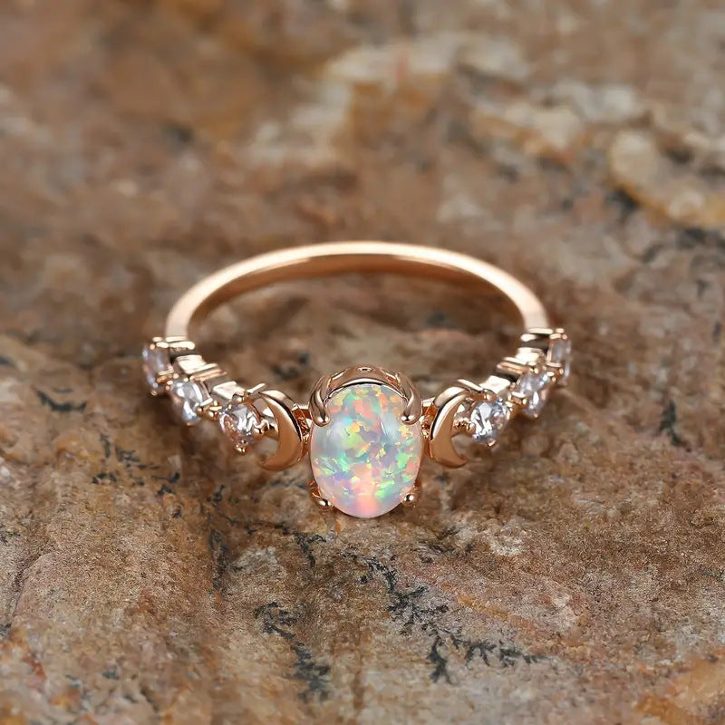 Rose gold-tone opal-style ring with crescent moon accents, top-down view on a stone surface