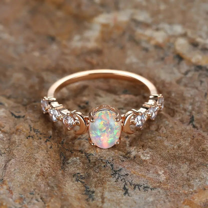 Rose gold-tone opal-style ring with crescent moon accents, top-down view on a stone surface