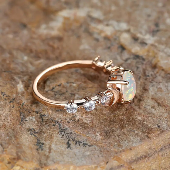 Side profile of a rose gold-tone ring showing the crescent moon accent and clear stones along the band