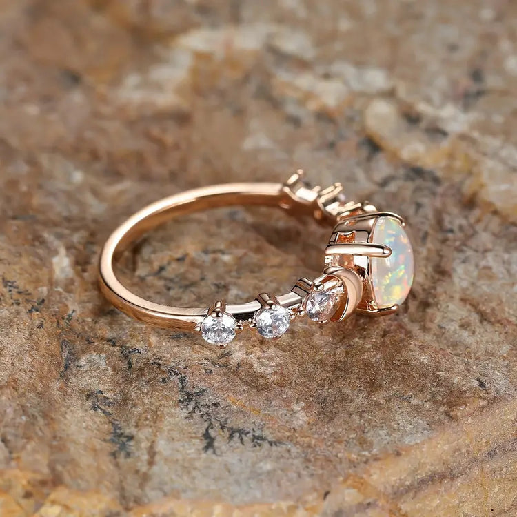 Side profile of a rose gold-tone ring showing the crescent moon accent and clear stones along the band