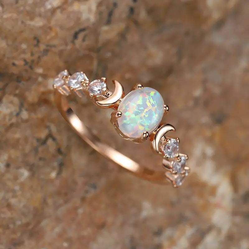 Close-up angled view of a rose gold-tone ring with an oval opal-style stone flanked by crescent moons