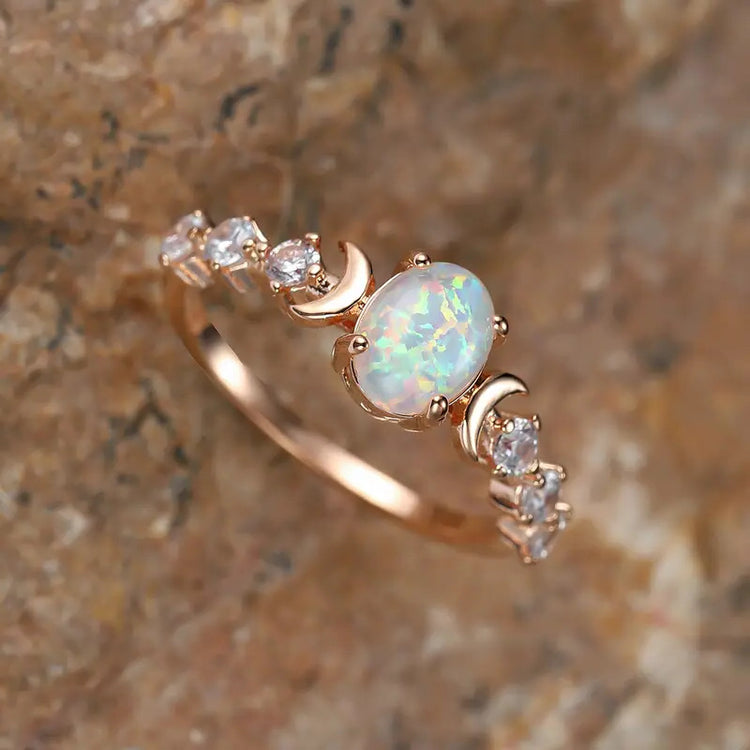 Close-up angled view of a rose gold-tone ring with an oval opal-style stone flanked by crescent moons